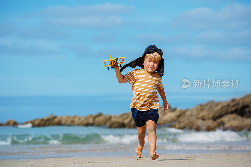 男孩戴着航空帽，带着玩具飞机模型在海滩上奔跑