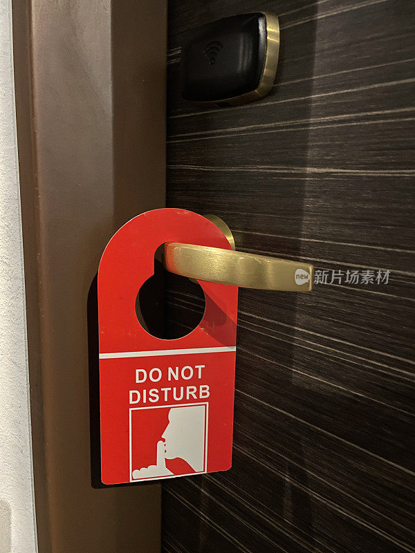打开的木质，酒店房间门的特写图像，门把手上挂着红色的“请勿打扰”标志，隐私请求标志，木纹背景，重点在前景