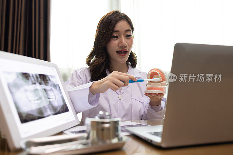 亚洲女牙医通过手提电脑与病人交谈，并建议如何刷牙