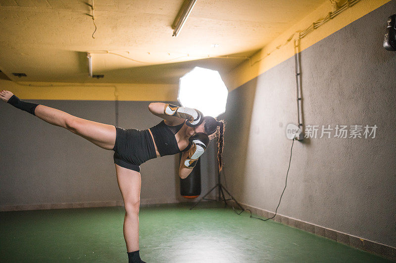 强壮的女子自由搏击运动员在健身房用拳击手套练习踢腿和出拳