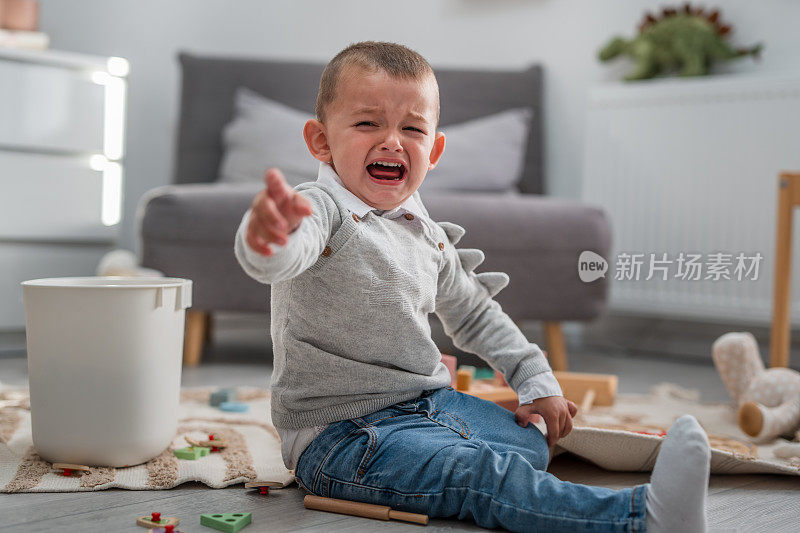 一个蹒跚学步的男孩坐在家里的地板上哭