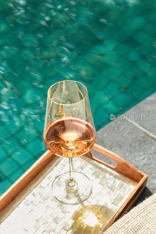 热带度假酒店游泳池木托盘上的玫瑰红酒杯