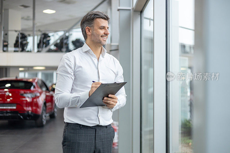 拿着剪贴板的人在汽车陈列室-销售员协助顾客购买新车