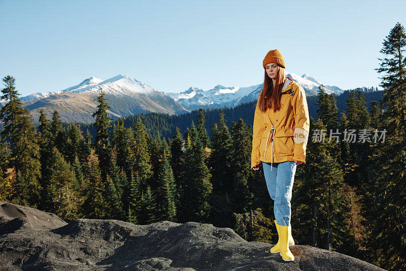 女人在丰满的笑容与牙齿幸福和笑声游客在黄色的雨衣站在山上旅行在秋天和徒步旅行在山上在夕阳的阳光自由