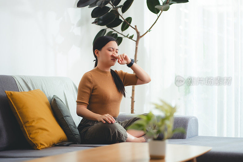 亚洲妇女发烧，流鼻涕，咳嗽和打喷嚏，坐在家里的沙发上。