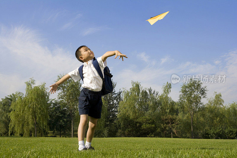 在草地上玩纸飞机的小男孩