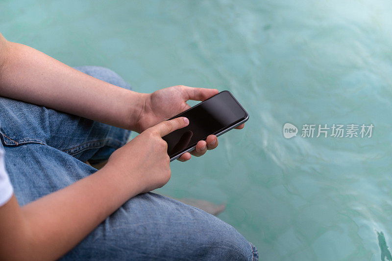 男子在泳池边用智能手机