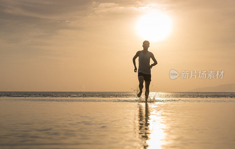 年轻的亚洲男子在海滩上奔跑，夕阳为背景