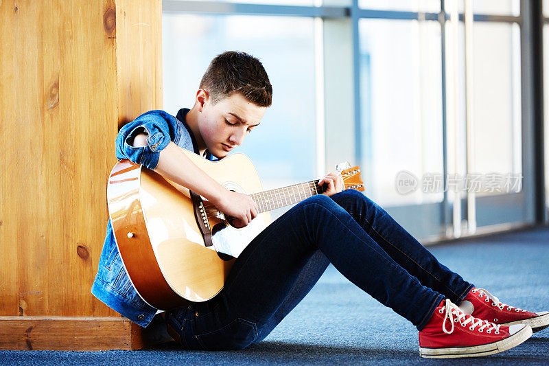 酷少年拿着吉他坐在走廊的地毯上