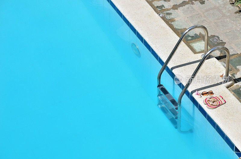 游泳池旁边的彩色人字拖和太阳镜