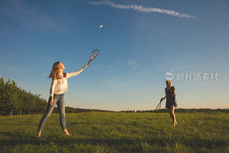 女性朋友在草地上对着天空打羽毛球