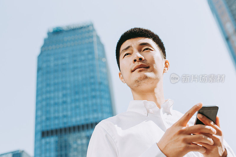 年轻的亚洲人在现代建筑附近使用手机