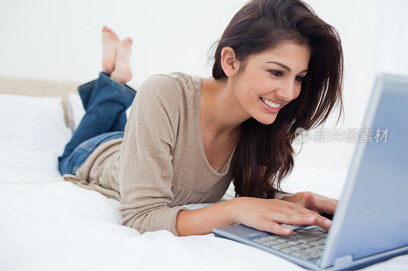 一个女人躺在床上，她的笔记本电脑在她面前，微笑着