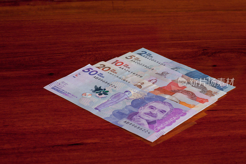哥伦比亚，南美洲——哥伦比亚的新钞票陈列在红木桌子上，按降序排列:上面有最高面额的钞票，上面印有诺贝尔奖得主加西亚·马尔克斯的肖像