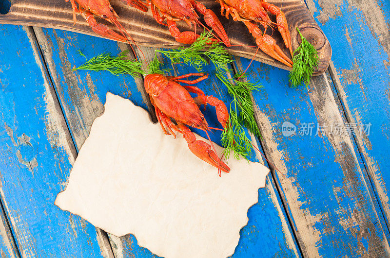 一只整只的红煮小龙虾，旁边是许多小龙虾，放在棕色的切菜板上，新鲜的绿色小茴香树枝，旁边是放在旧的乡村蓝色木板上的空烤盘