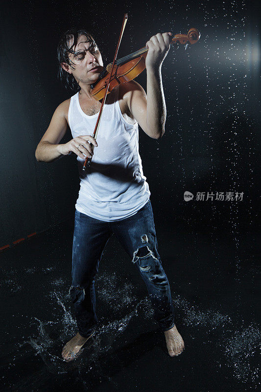 穿着牛仔裤的音乐家男孩在雨中拉小提琴