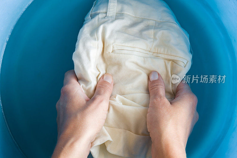 主妇的手在蓝色的盆子里洗浅短裤。干洗的概念。衣服护理。女仆的家务。定期清洗。