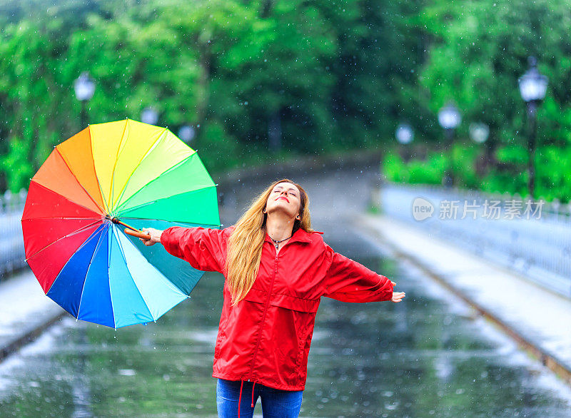 快乐的年轻女子撑着雨伞在雨中行走