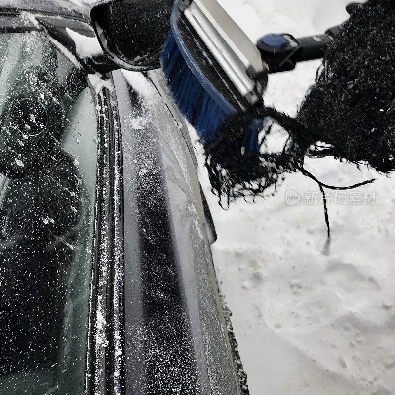 一位老妇人在下雪天用雪刷清洁她的车。