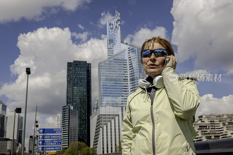 法国巴黎，塞纳河河畔的拉德芳斯，一个成熟的女人在跑步中使用手机