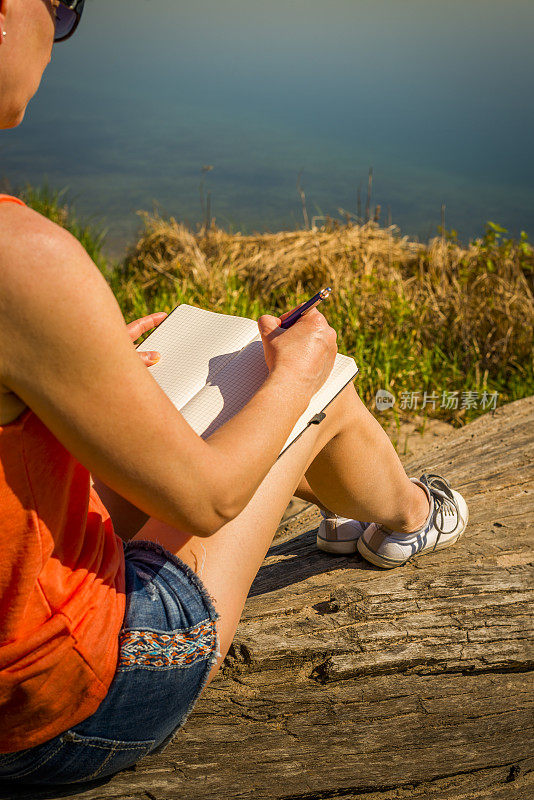 年轻女子坐在湖边写日记