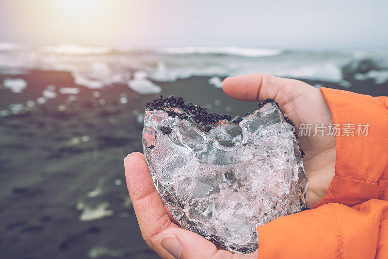 在冰岛Jokulsarlon的黑色沙滩上，手持冰的人对景观的特写