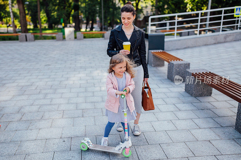 一个学龄前的小女孩在现代城市环境中骑着滑板车