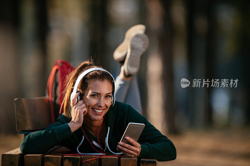 年轻的女运动员在大自然中听音乐