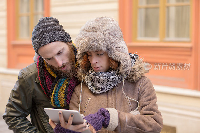 戴着冬季帽子的年轻夫妇在平板电脑上浏览街道指示