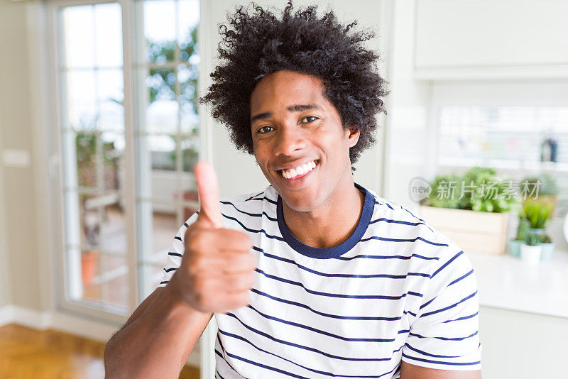 非裔美国人穿着条纹t恤做快乐的拇指手势与手。赞许的表情看着镜头，表示成功。