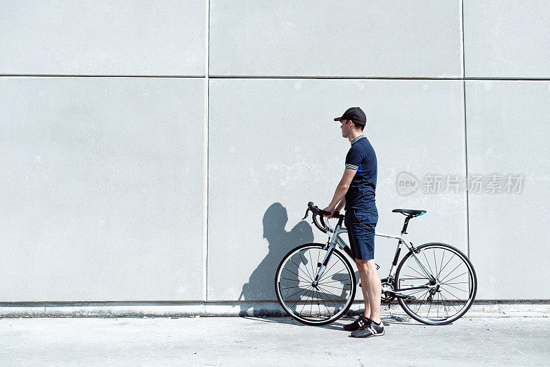 肖像骑自行车的人站在他的公路自行车看着混凝土墙