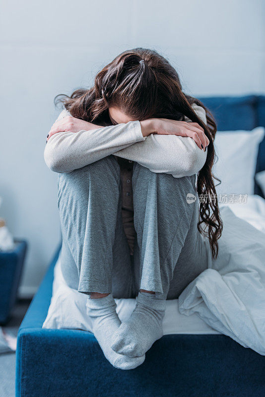 抑郁的女人头向下抱着膝盖坐在家里的床上