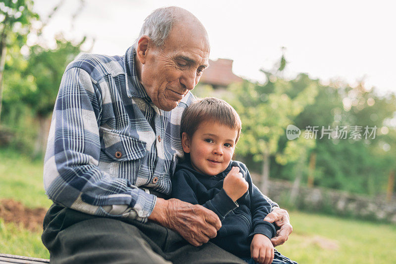 爷爷坐在长椅上，拥抱着他可爱的孙子。
