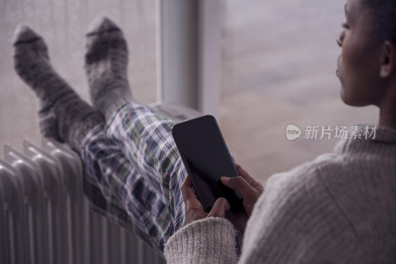 一位女士在电暖器前用智能手机加热腿。