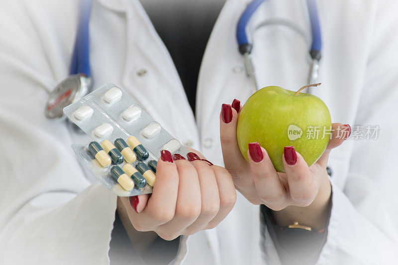 近距离拍摄的一个身份不明的医生拿着一个苹果和各种药丸在她的手中