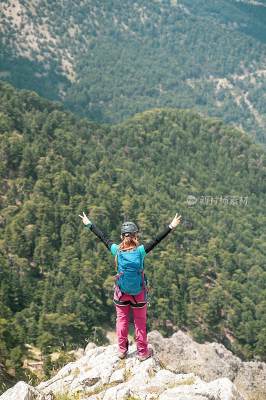 一位女性高山攀岩者正在山顶做和平手势