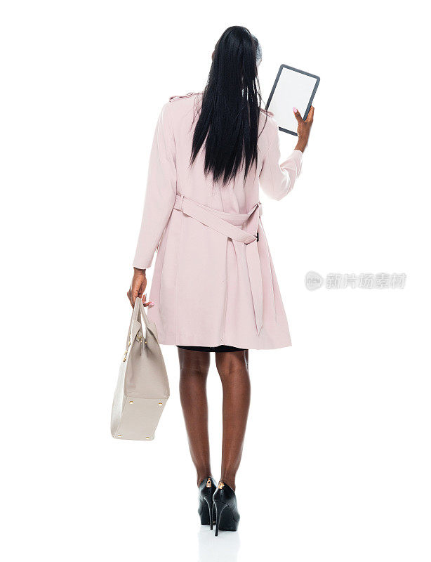 非裔美国年轻女性穿着风衣站在白色背景前，拿着钱包，使用触摸屏