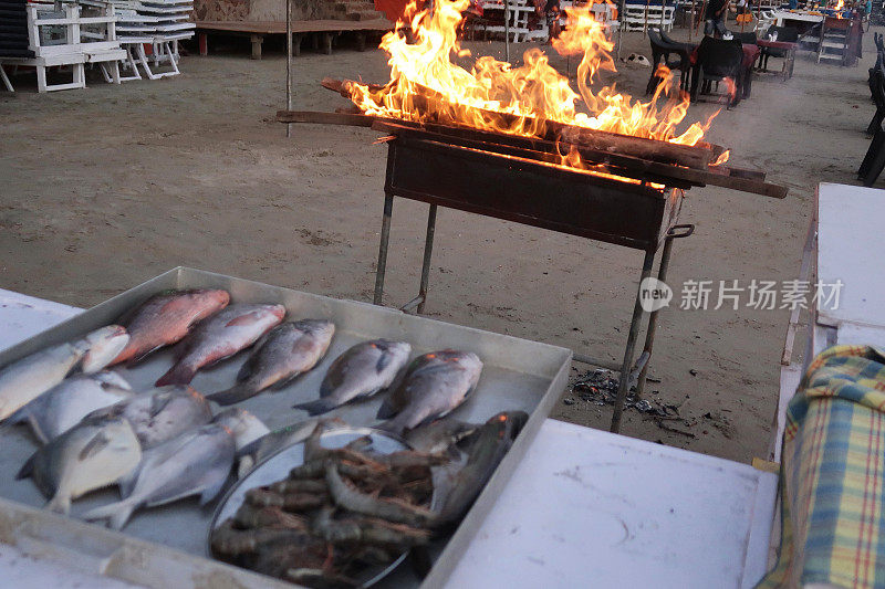 整条鱼和对虾装在金属托盘里，准备放在海滩烧烤架上，户外海滩餐厅，火焰烧烤