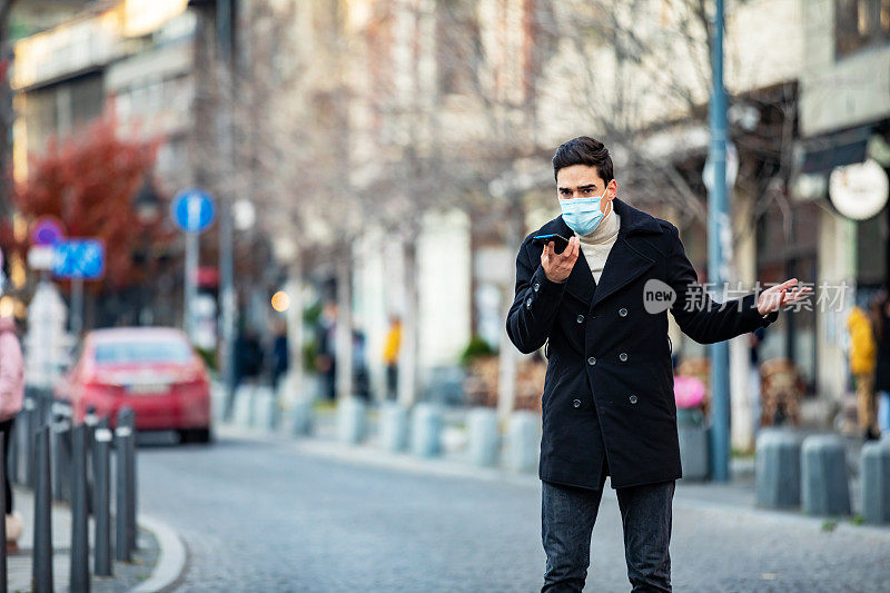 商人在街上戴着防护口罩，以避免COVID-19和使用手机