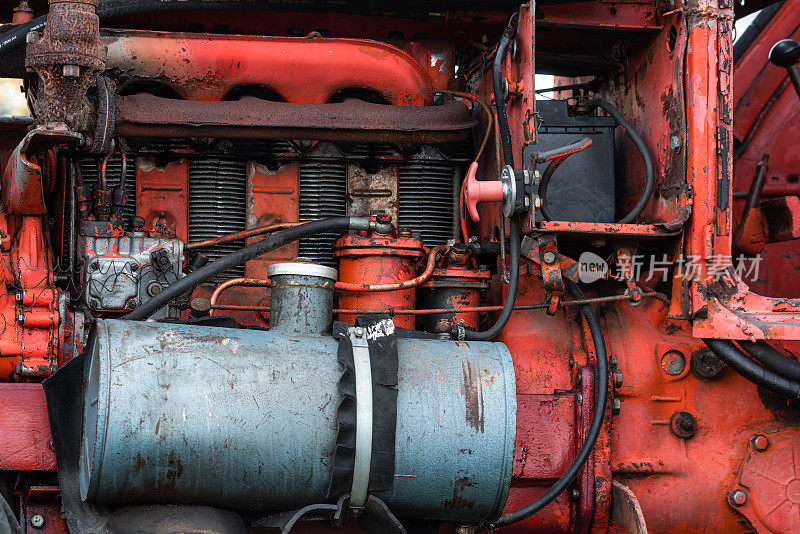 在阳光明媚的秋日保加利亚农村，旧的银色柴油坦克上红色的老式俄罗斯拖拉机发动机可见电线生锈和油滴