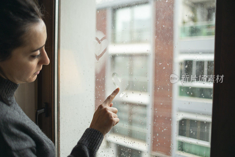 快乐的女人在雨天的窗户上画一颗心