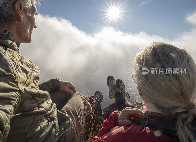 早晨，成熟的情侣徒步旅行者在长满草的山坡上放松