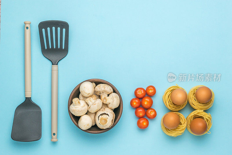 蓝色背景上的两把厨房抹刀，意大利面，鸡蛋，蘑菇和西红柿。