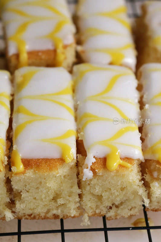 这是自制柠檬盘烤蛋糕片的特写，上面覆盖着白色的方糖糖霜和羽毛状的黄色柠檬味糖霜，放在金属冷却架上，聚焦前景，俯瞰高处