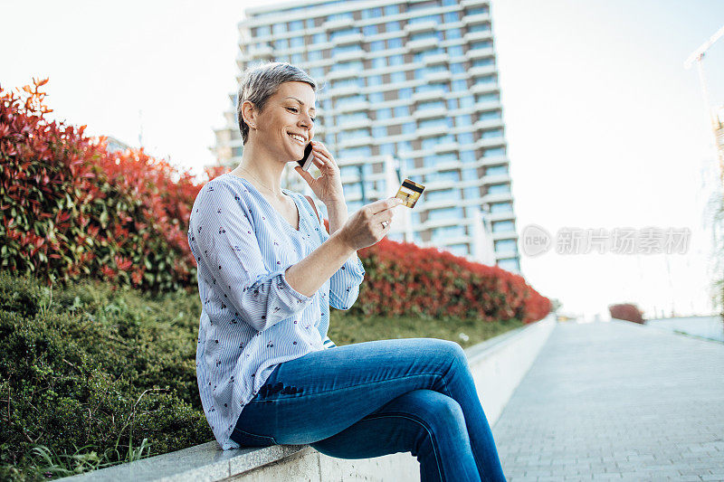 快乐的女人在城市里休息，通过一个电话银行