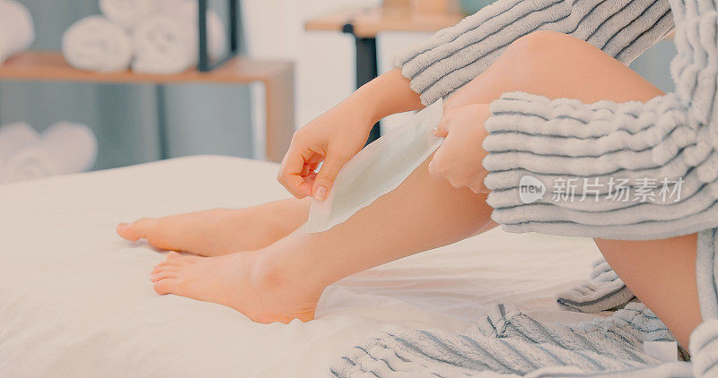 一个不知名的女人独自坐在水疗中心的床上给她的腿打蜡