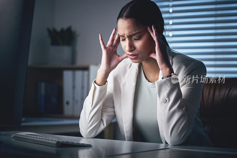 一个迷人的年轻女商人晚上独自坐在办公室里，忍受着头痛的折磨