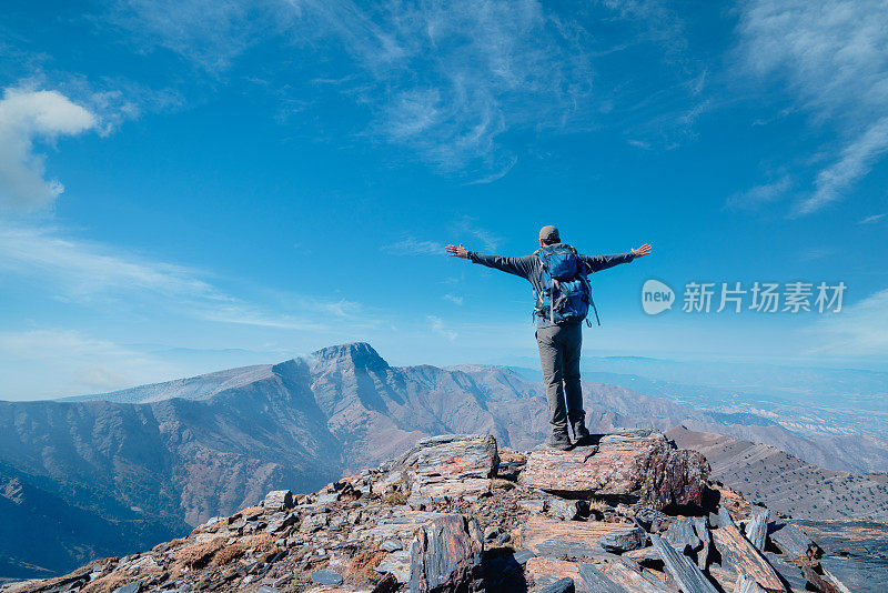 成功的登山者在山顶自信地张开双臂欣赏风景