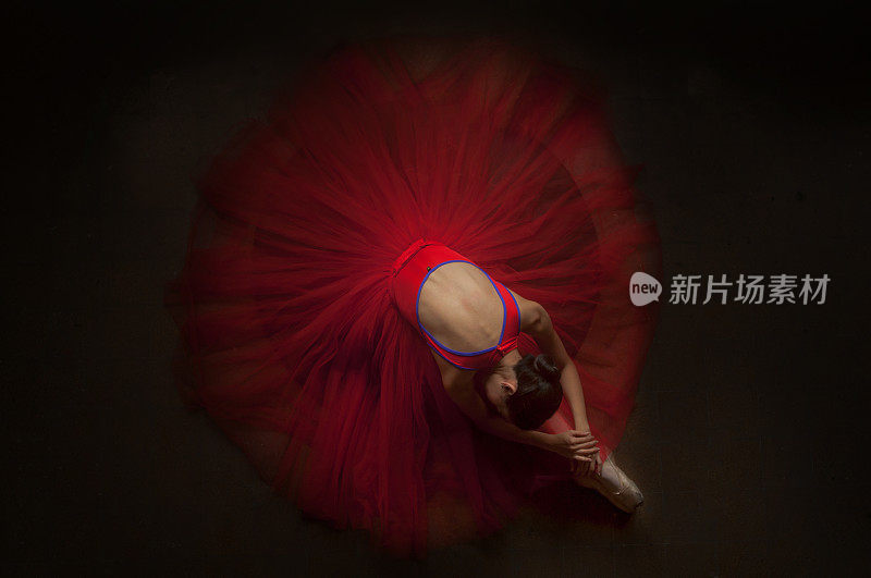 美丽的芭蕾舞女演员躺在她的膝盖上，穿着美丽的红色短裙