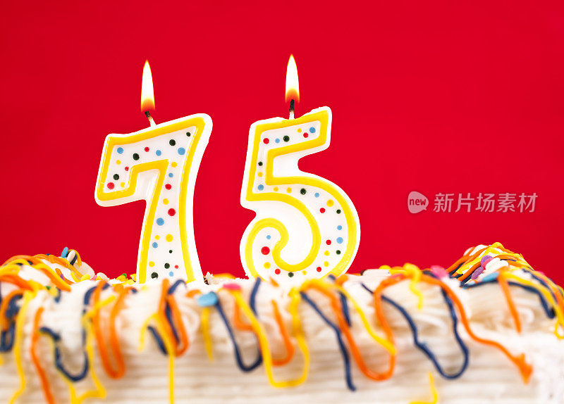用75号燃烧的蜡烛装饰生日蛋糕。红色的背景。
